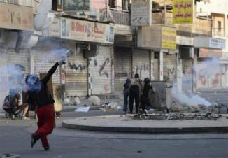 A protester throws a tear gas canister back at riot police during clashes taking place during a protest over the death of detainee Jaffar Mohammed Jaffar at a hospital, ahead of his funeral in the village of Daih, west of Manama