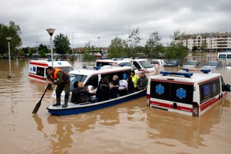 Serbian rows a boat past flooded ambulance vehicles in the flooded town of Obrenovac